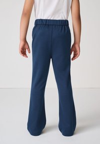 Pantalones de mezcla de algodón azul marino con una cintura elástica, piernas acampanadas y una textura suave, mostrados desde atrás, sin bolsillos visibles.