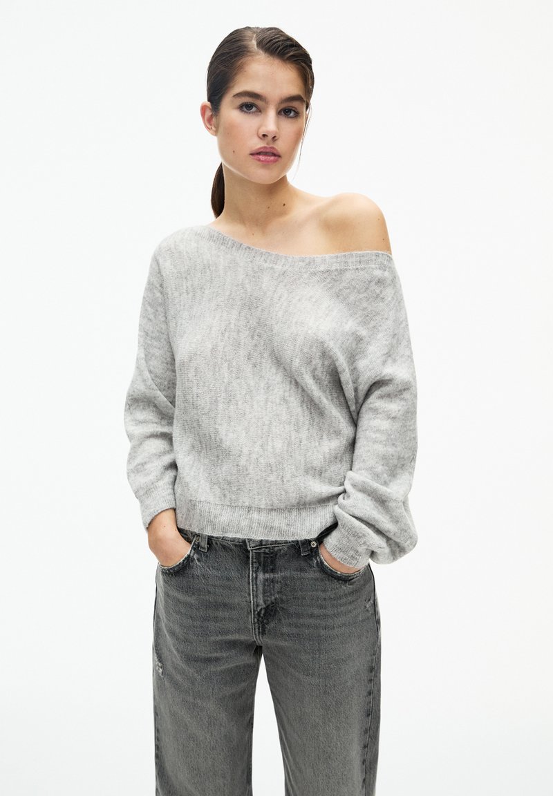 Maglione grigio chiaro, lavorato a maglia, con design off-shoulder, maniche lunghe e orlo a coste, abbinato a jeans grigio scuro a vestibilità rilassata.