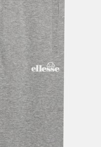 Šedé tepláky s texturovanou tkaninou, elastickým pásom a bielym logom "ellesse" na ľavej strane. Jednoduchý a ležérny dizajn.