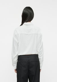 Camisa blanca de manga larga con cuello, con una textura suave. Combinada con pantalones negros, que presentan un corte clásico y relajado.