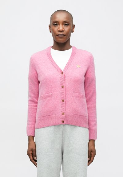 Roze gebreide cardigan met een V-hals, knoopsluiting, zakken en een kleine gouden accent. Zachte textuur en geribbelde details aan de randen.