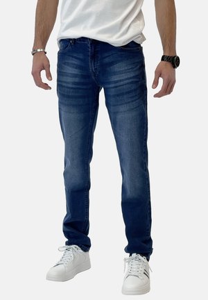 Jeans in denim blu scuro con vestibilità slim, caratterizzati da leggere sfumature e dettagli sbiaditi. Abbinati a sneakers bianche per un contrasto.
