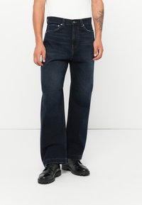 Dark blue wide-leg denim jeans with five pockets, button closure, and subtle detailing; paired with black lace-up ankle boots.