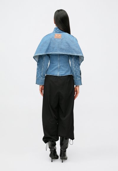 Džinsa jaka ar īsu siluetu, gaiši zila krāsa, plats apkaklis un smalks raksts uz piedurknēm, kopā ar melnām vaļīgām biksēm un zābakiem.