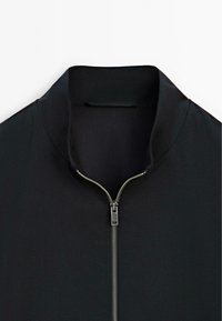 Black zip-up jacket with a high collar, featuring a metallic zipper and smooth fabric texture. Simple design, without patterns or embellishments.