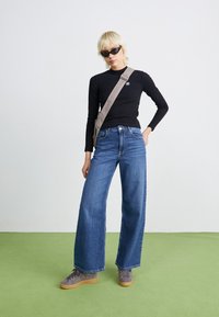 Svart langermet topp, lys grå crossover-veske, vide blå jeans og grå joggesko. Glatt denimtekstur og uformell design.