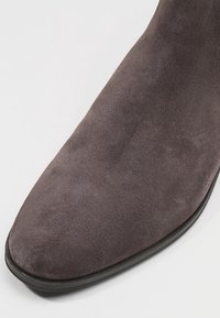 Bottine en daim gris à bout pointu et texture lisse, avec une semelle noire, mettant en valeur son design élégant et minimaliste.