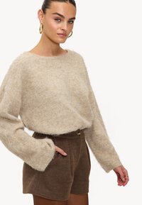 Pull beige doux avec des manches larges, associé à un short marron avec une fermeture à bouton. Le pull a une coupe décontractée et une texture douce.
