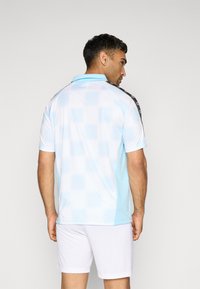 Hemd met korte mouwen in lichtblauwe kleur met een patroon, voorzien van een contrasterend zwart schouderontwerp, gecombineerd met witte shorts.
