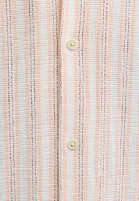 Κοντινό πλάνο υφάσματος με κάθετες ρίγες σε πορτοκαλί, λευκό και καφέ χρώμα και δύο ραμμένα κουμπιά σε εκρού απόχρωση.