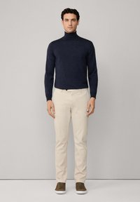 Granatowy sweter z golfem w połączeniu z beżowymi spodniami i brązowymi trampkami. Gładka faktura i dopasowany krój z prostą, czystą sylwetką.