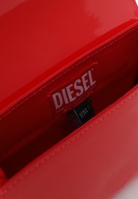 Portefeuille en cuir verni rouge avec une texture lisse. L'intérieur présente un revêtement en tissu rouge et une étiquette logo visible, indiquant la marque et le modèle.