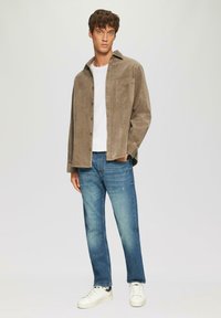 Bruine corduroy knoopshirt met een zak, gecombineerd met lichtblauwe rechte jeans en witte sneakers. Eenvoudig, gestructureerd ontwerp.