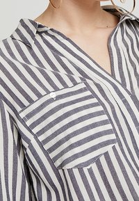 Camicia a righe a maniche lunghe in crema e blu navy. Presenta una tasca sul petto, colletto e tessuto leggero con vestibilità comoda.