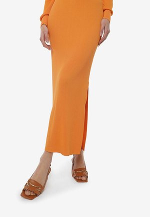 Vestido maxi naranja de canalé con una abertura lateral y mangas largas, combinado con sandalias marrones de punta cuadrada con detalles de cadena.