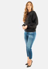 Suéter negro de felpa con un acabado texturizado, jeans ajustados azules y zapatos de tacón negros. Presenta un cuello redondo y mangas largas.
