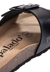 Sandale en cuir noir avec une large lanière et une boucle ajustable. Dotée d'une semelle intérieure en daim beige et d'une semelle en liège texturé pour plus de confort.