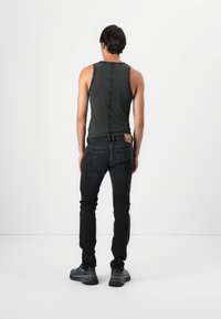 Top negru fără mâneci cu detalii cusute, purtat cu blugi închiși și adidași negri. Spatele topului are un design cu o cusătură centrală.