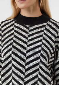 Czarnobiały sweter w paski z prążkowanym dekoltem, z wzorem w jodełkę i fakturowaną tkaniną. Zbliżenie górnej części ubrania.