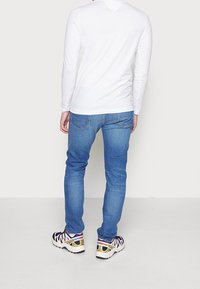 Camicia bianca di cotone a maniche lunghe, jeans in denim blu e scarpe da ginnastica multicolori con suola testurizzata. Vista posteriore dell'abbigliamento.