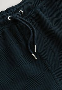 Joggers texturés sombres avec un motif en chevrons, taille élastique et cordon de serrage avec embouts en métal.