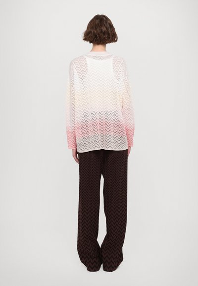 Pulover ușor, cu tricotare deschisă, cu un gradient de la alb la roz, având un model în zigzag. Asortat cu pantaloni largi maro, tot cu model în zigzag.