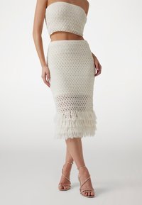 Ensemble en crochet blanc composé d'un top sans bretelles et d'une jupe mi-longue avec un ourlet à franges. Texture lisse, design en tricot ouvert.