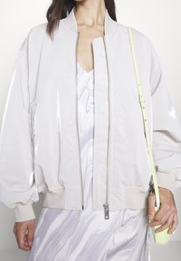 Lehká bomber bunda světle růžové barvy s lesklým povrchem, žebrovanými manžetami a zipem. Malá neonově žlutá taška doplňuje vzhled.