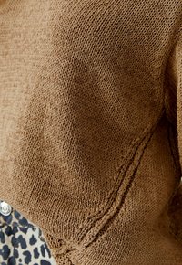Brauner Strickcardigan mit strukturiertem Finish und offener Gestaltung, sichtbaren Nähdetails und lässiger Passform.