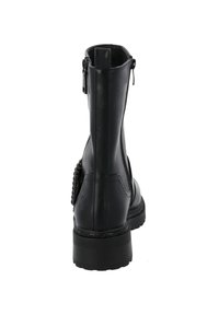Botín de cuero negro con cierre de cremallera, parte trasera texturizada y suela gruesa. Presenta un adorno de hardware decorativo cerca del talón.