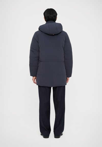 Padded mornarski parka s kapuljačom, s prešanim dizajnom i dugim rukavima, nosi se s mornarskim hlačama s prugama, prikazano s leđa.
