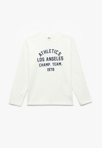 Biała koszula z długim rękawem z bawełny, z niebieskim textem "ATHLETICS LOS ANGELES CHAMP. TEAM. 1978" w pogrubionym drukowanym stylu.