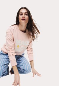 Felpa rosa chiaro con grafiche "PACE & AMORE", abbinata a pantaloni a righe blu e bianche, che mostrano un fit rilassato e una texture morbida.