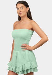 Mintgroene strapless jurk met een gestructureerde, gekreukte stof, een aansluitend lijfje en een uitlopende rok met ruches aan de zoom.