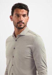 Lichtgrijze lange mouwen knoopsluiting shirt met een kraag, met een gladde structuur en donkere knopen die langs de voorkant zijn uitgelijnd.