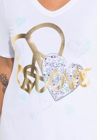 Camiseta blanca de manga corta con un signo de paz dorado, un corazón con patrones florales y la palabra "amor" en letras doradas.