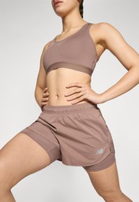 Soutien-gorge de sport marron avec un short assorti, présentant un design sans couture, une taille élastique et un logo discret sur le short. Texture lisse.