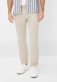 Light beige linen trousers with a straight fit, cuffed hems, and a front button closure, paired with white athletic shoes.