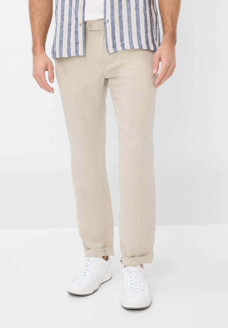 Light beige linen trousers with a straight fit, cuffed hems, and a front button closure, paired with white athletic shoes.