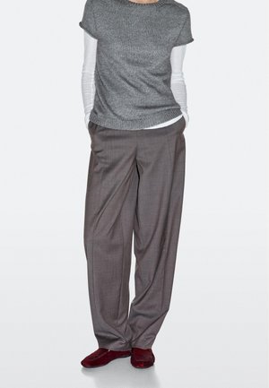 Grå kortærmet striktrøje lagdelt over en hvid langærmet skjorte, kombineret med løstsiddende, grå ternede bukser og røde slip-on sko.