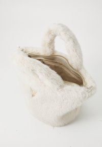 Petit sac à main en fausse fourrure couleur crème avec des poignées arrondies et une fermeture éclair dorée partiellement ouverte, révélant un intérieur en tissu beige avec une poche zippée.