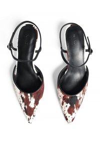 Punkt-veidīgi smaili papēži ar melnas ādas akcentiem un baltu un brūnu pleķainu govs ādas virspusi. Gluda iekšējā tekstūra, regulējama siksna.