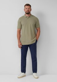 Oliwkowa koszulka polo z krótkim rękawem zestawiona z granatowymi spodniami i białymi sneakersami. Posiada klasyczny kołnierzyk i dopasowany krój.