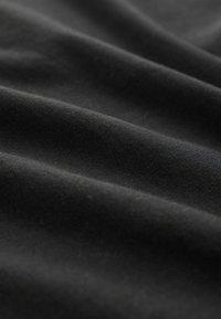 Tessuto di cotone nero con una texture liscia, caratterizzato da pieghe sottili e una finitura opaca, che mostra un colore uniforme e un minimalismo nei dettagli.