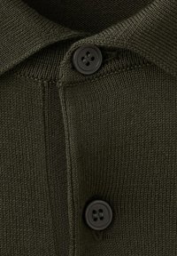 Ciemnozielona dzianina z dwoma czarnymi, czterodziurkowymi guzikami ułożonymi pionowo oraz widocznymi detalami szwów na listwie.