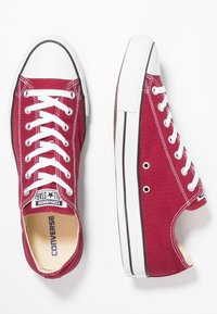 Rote Leinensneaker mit weißen Schnürsenkeln, gummierter Zehenschutzkappe und schwarzem Rand. Sie haben eine flache Sohle und ein Sternlogo auf der Zunge.