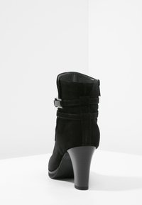 Bottines en suede noir avec un talon haut, fermeture éclair sur le côté et une sangle réglable avec une boucle en métal à l'arrière.