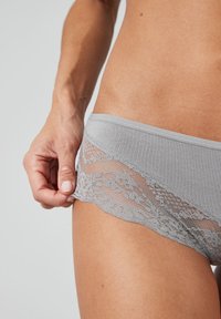Lichtgrijze onderbroek van ribstof met bloemenkant langs de randen, wat de soepele textuur en zachte uitstraling benadrukt.