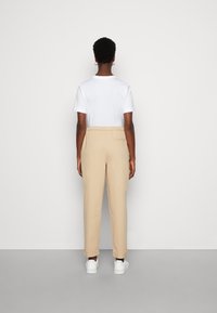 Khaki broek met elastische tailleband, taps toelopende pasvorm en zijzakken, gecombineerd met een plain wit T-shirt en witte sneakers.