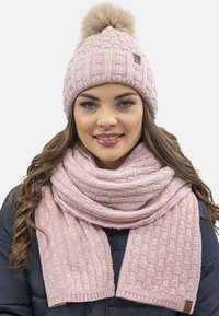 Cappello di lana rosa con pom-pom in pelliccia sintetica e sciarpa coordinata con texture. Entrambi gli articoli presentano un motivo intrecciato e una texture morbida e calda.